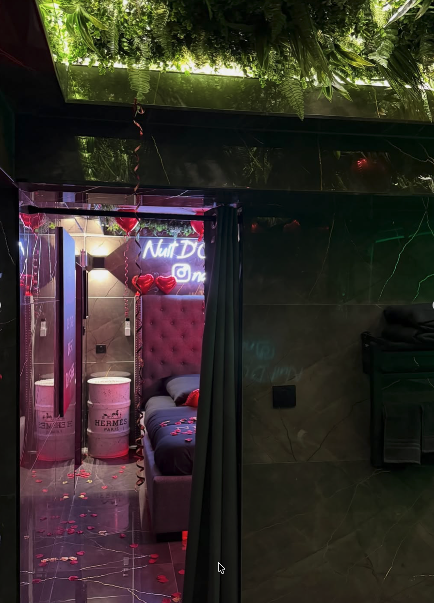 Entrée de la suite sous un plafond végétal, avec vue sur le lit et le néon Nuit d’Or